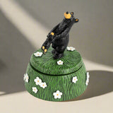 Decorative box with a black bear on top, surrounded by flowers on a white background