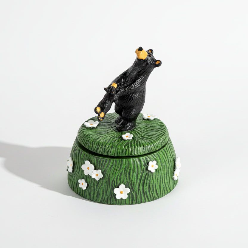 Decorative box with a black bear on top, surrounded by flowers on a white background