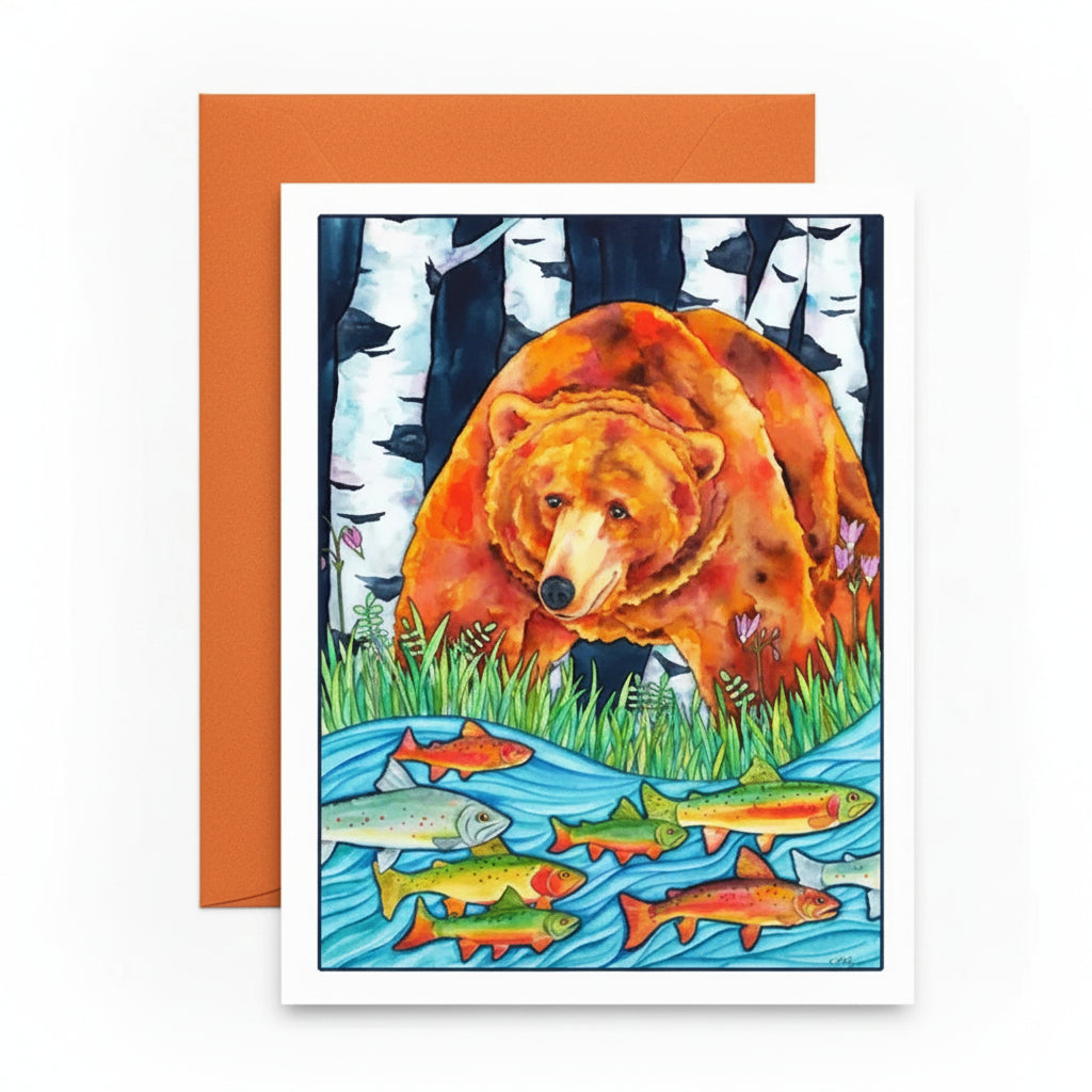A square art print or greeting card featuring a colorful illustration of a brown bear standing in a stream with fish, placed in front of an orange envelope on a white surface.