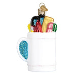 Decorative glass ornament of a mug with colorful items on a white background