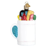 Decorative glass ornament of a mug with colorful items on a white background