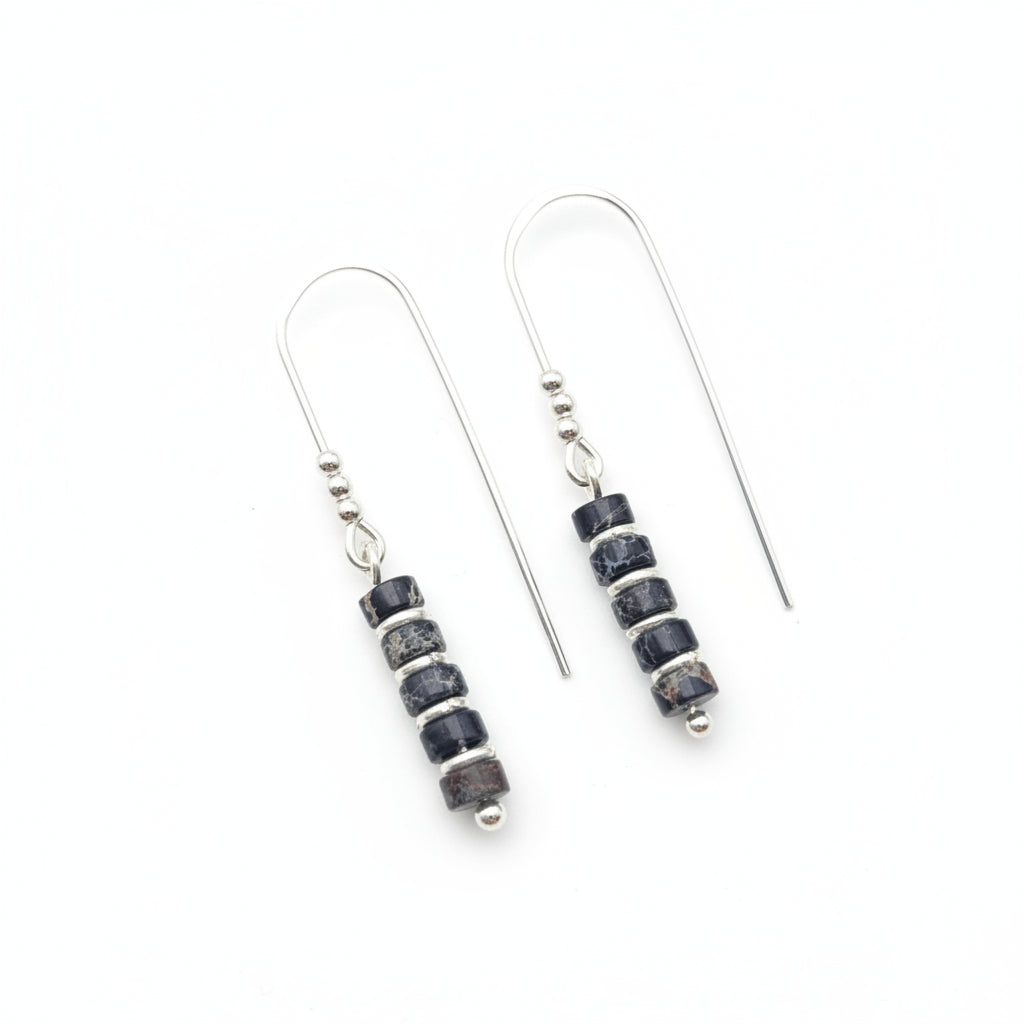 A pair of silver fishhook drop earrings with a cluster of dark blue and black stone beads separated by small silver spacer beads, displayed on a textured white surface.