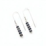 A pair of silver fishhook drop earrings with a cluster of dark blue and black stone beads separated by small silver spacer beads, displayed on a textured white surface.