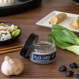 Assorted Asian cuisine including dumplings, sushi, and black garlic on a wooden table.