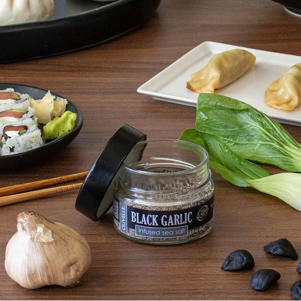 Assorted Asian cuisine including dumplings, sushi, and black garlic on a wooden table.