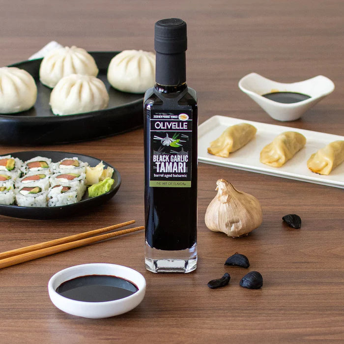 Olivelle Black Garlic Tamari bottle on a wooden table with sushi and other food items.
