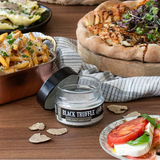 Table with food including a pizza, pasta, salad, and a jar of black truffle oil.