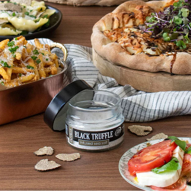 Table with food including a pizza, pasta, salad, and a jar of black truffle oil.