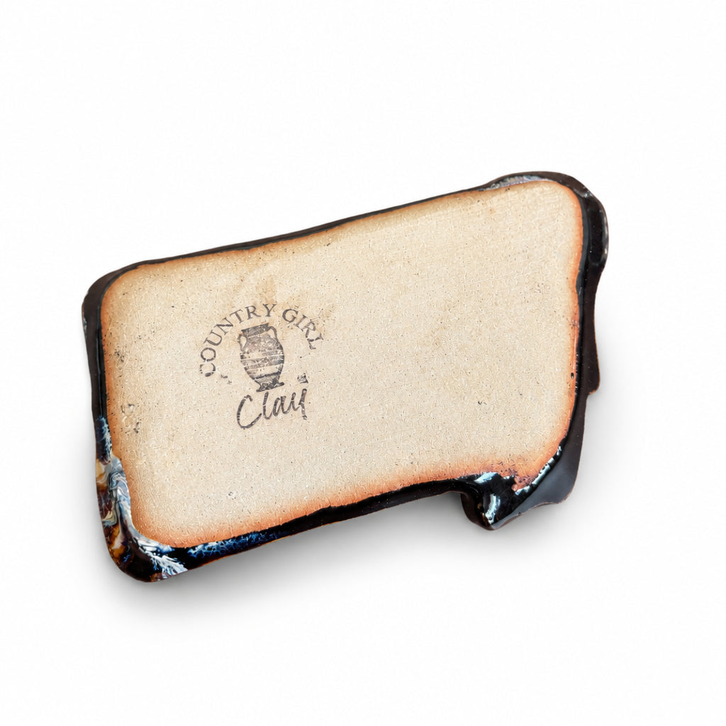 back of a Montana shaped ceramic dish with a glossy black glaze, featuring a marbled pattern of white, blue, and brown swirls, and a rustic copper-brown rim, shown on a plain white background.