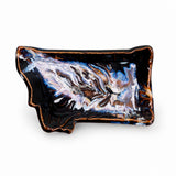 An Montana shaped ceramic dish with a glossy black glaze, featuring a marbled pattern of white, blue, and brown swirls, and a rustic copper-brown rim, shown on a plain white background.