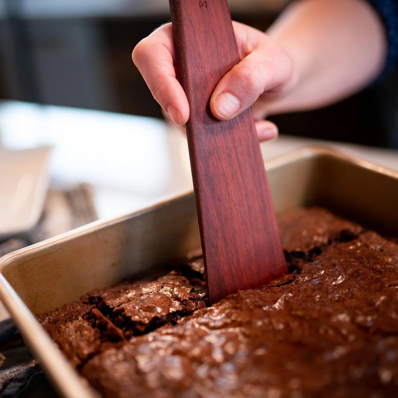 Hand using a wooden spatula to cut brownies from a baking pan.