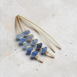 A pair of gold-toned dangle earrings with blue faceted beads and small gold spacer beads, displayed on a light textured surface.
