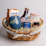 Gift basket with a blue mug, cookies, and other snacks on a light gray background