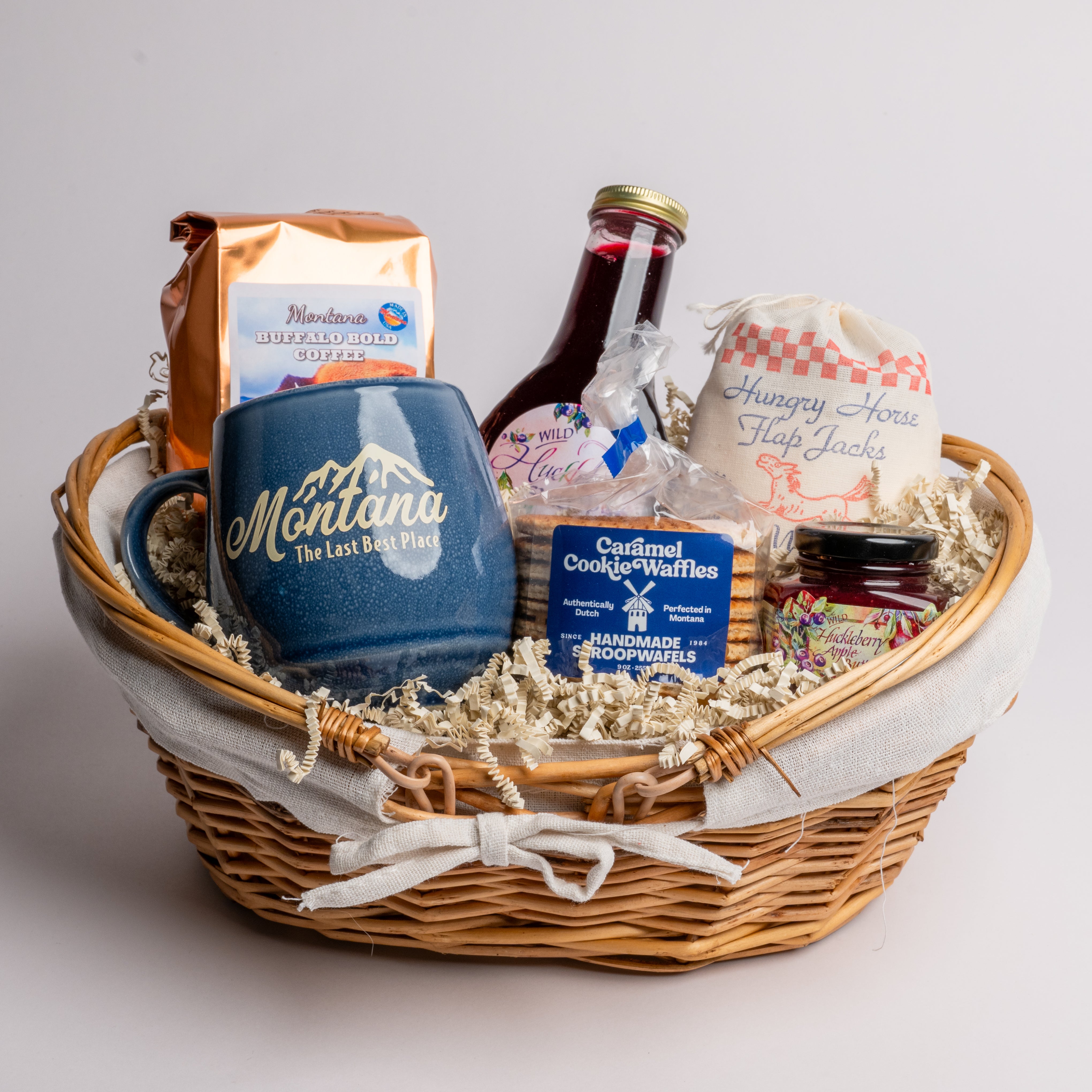 Gift basket with a blue mug, cookies, and other snacks on a light gray background