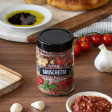 Jar of Olivelle Bruschetta seasoning on a wooden table with ingredients and bread.
