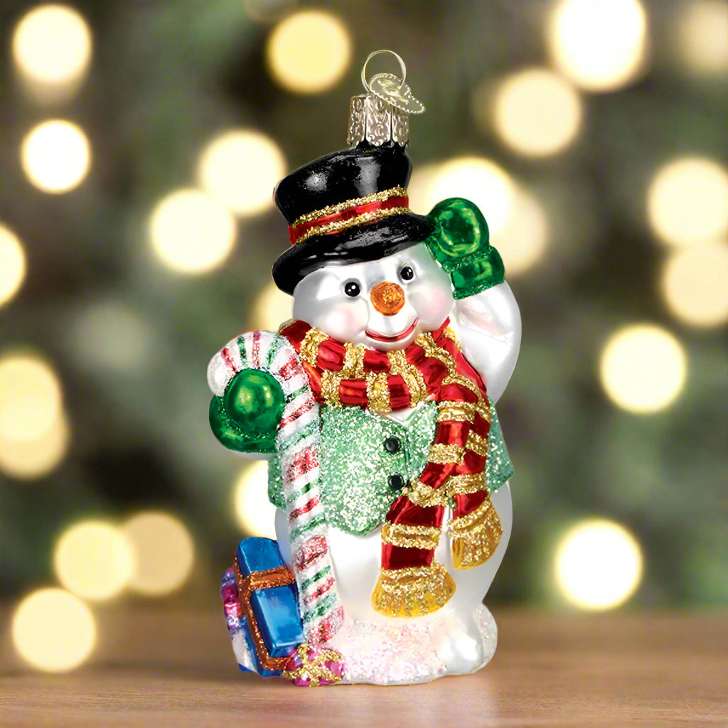 Glass snowman ornament with candy cane, top hat, and scarf on a white background