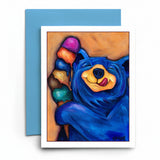 A greeting card featuring a colorful painted blue bear holding an ice cream cone, shown with a light blue envelope on a white background.