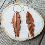 Feather-shaped earrings with gold chains on a wooden surface