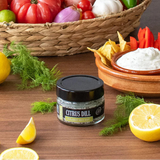 Jar of citrus dill seasoning with lemons, herbs, and a bowl of dip on a wooden surface.