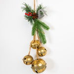 Decorative hanging with gold jingle bells, greenery, and pinecones on a white background
