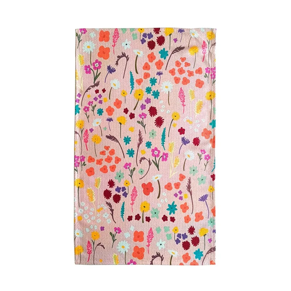 A rectangular woven textile, likely a tea towel or small blanket, featuring a dense, colorful wildflower pattern on a light pinkish-beige background. The design includes flowers and leaves in orange, yellow, red, pink, blue, and purple, set against a plain white background.