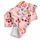 A pink tea towel with a colorful floral print, laid flat on a white surface.