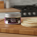 Olivelle Cumin & Garlic Taco rub & seasoning container on a wooden cutting board with tortillas.