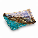 A handmade ceramic dish with a textured, organic shape. The top surface features a purple and blue glaze with a raised bubble pattern, while the outer edge has a turquoise blue textured glaze with gold-colored edging, all set against a clean white background.