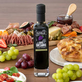 Bottle of Olivelle Dark Balsamic vinegar on a wooden table with food platter