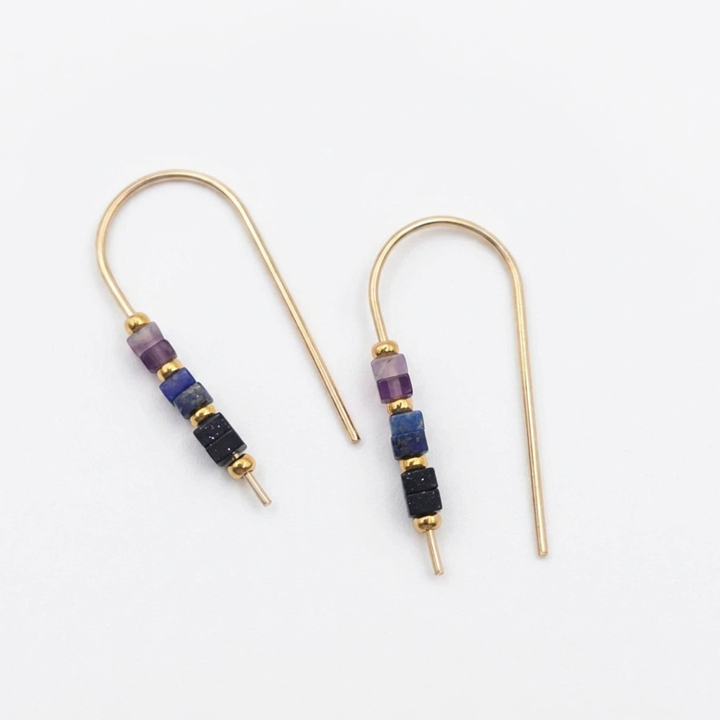 A pair of gold-tone drop earrings with small cylindrical beads in purple, blue, and black, displayed on a clean white background.