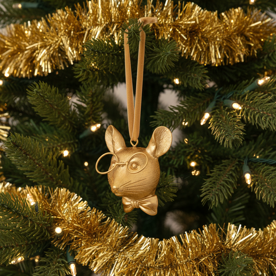 Gold mouse ornament with glasses and a bow tie on a Christmas tree.