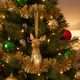 Gold deer ornament on a decorated Christmas tree with green and red ornaments.