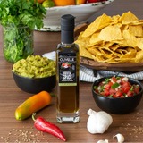 Olivelle Fiesta Spice infused olive oil bottle on a table with chips, guacamole, and salsa.