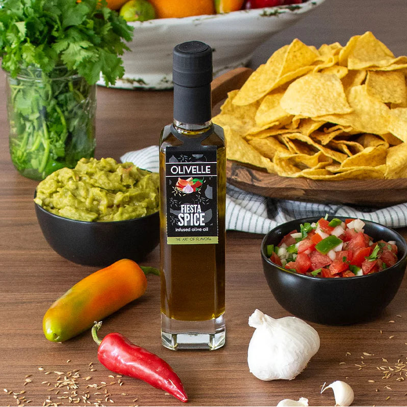 Olivelle Fiesta Spice infused olive oil bottle on a table with chips, guacamole, and salsa.