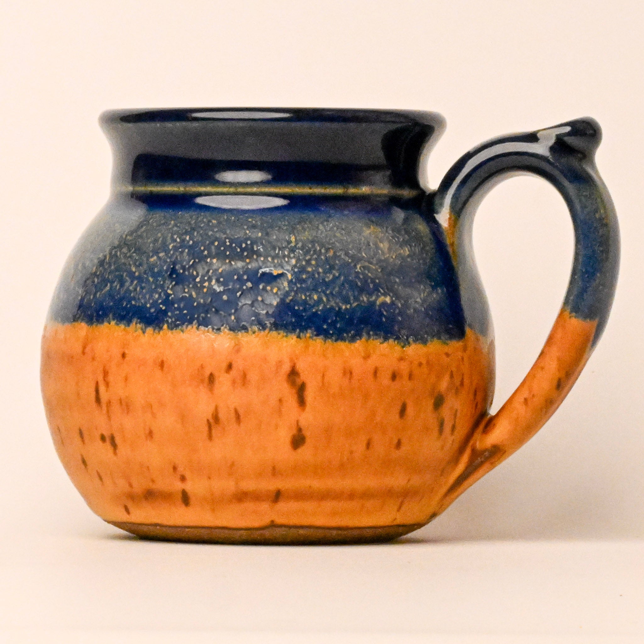 Ceramic mug with blue and orange glaze on a beige background