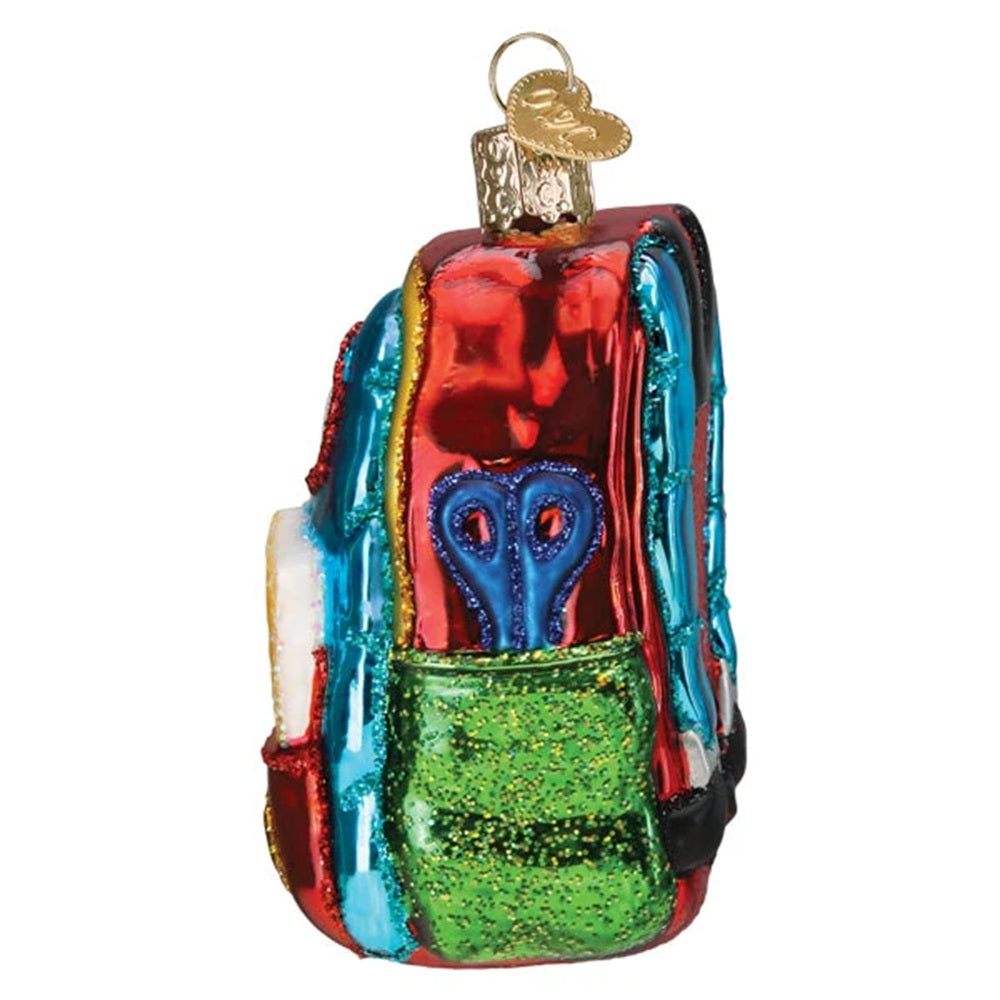 A colorful, backpack-shaped Christmas ornament with a metallic, reflective finish. It features a red top section, a green front pocket, blue scissors in the center, and a gold hanging loop at the top, shown against a plain white background.