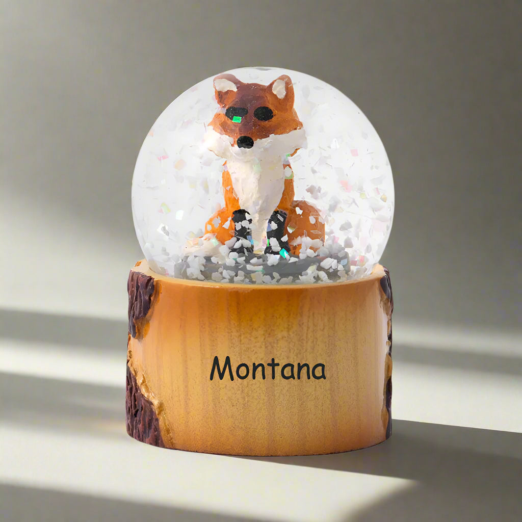 Snow globe with a fox figure on a wooden base labeled 'Montana' against a white background