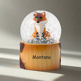 Snow globe with a fox figure on a wooden base labeled 'Montana' against a white background