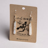 A pair of white pearl dangle earrings on a brown kraft display card with a black bird illustration and the text Lady Bird, Bozeman, MT, Ladybirdmk.com, photographed against a light gray background.
