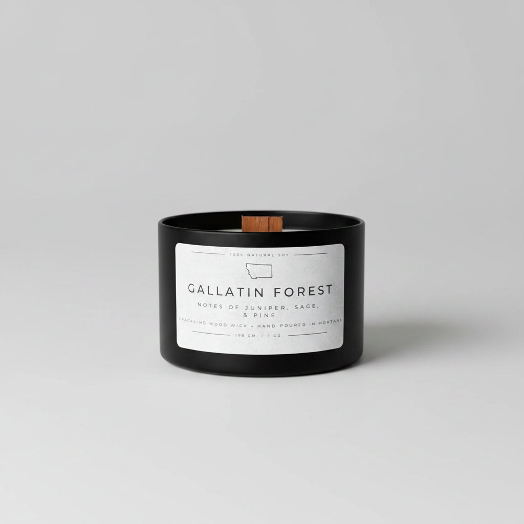 Black candle labeled 'Gallatin Forest' on a wooden surface with a blurred green background