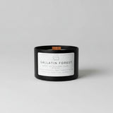 Black candle labeled 'Gallatin Forest' on a wooden surface with a blurred green background