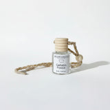 A small clear glass bottle with a white label reading 'Gallatin Candle Co. Gallatin Forest' and a light wood stopper, tied to a braided beige cord with a wooden bead, on a white background.