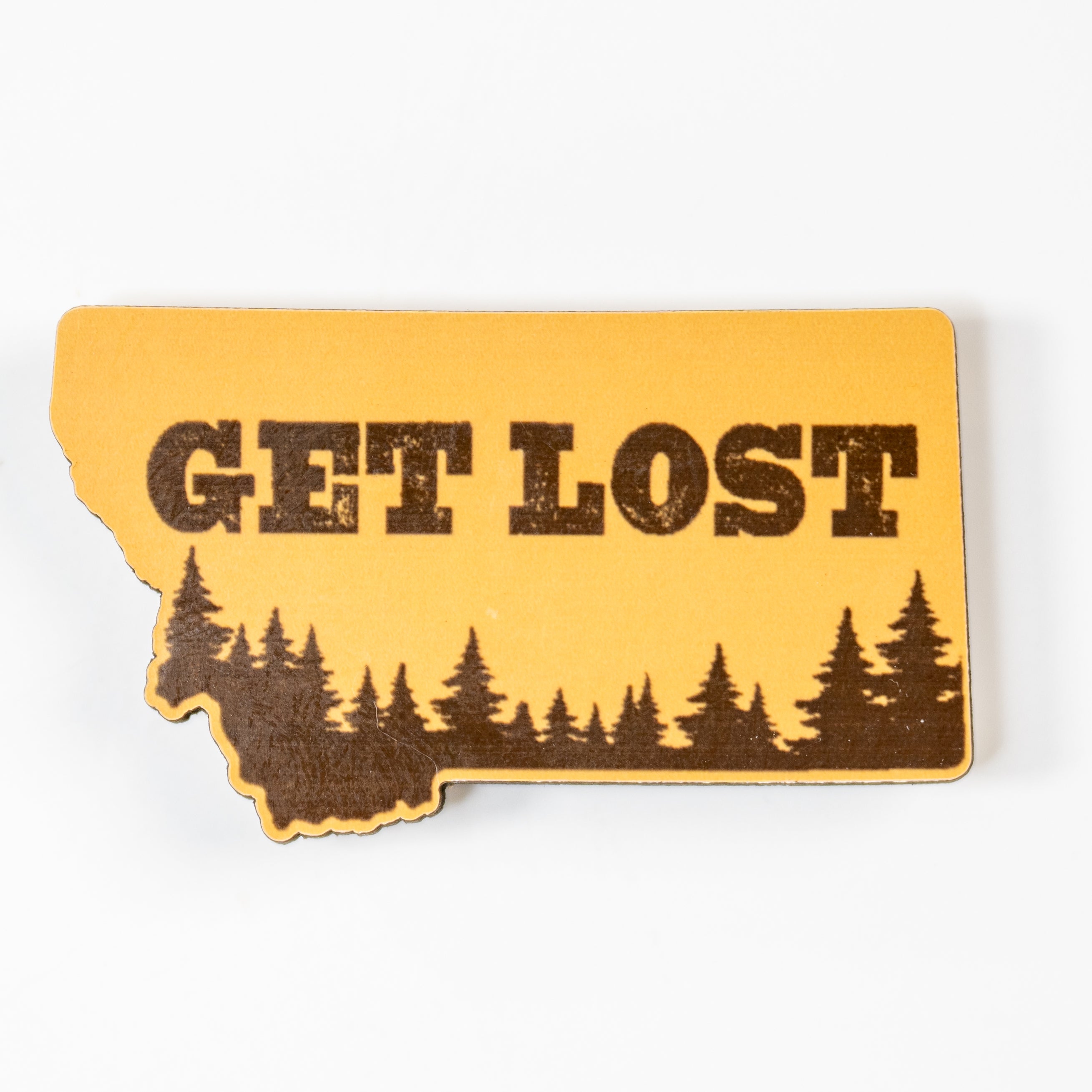 Yellow magnet shaped like the state of Montana with 'GET LOST' text and forest design on a white background