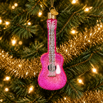 A pink glitter ukulele Christmas ornament hanging on a decorated Christmas tree with gold tinsel and warm white lights.