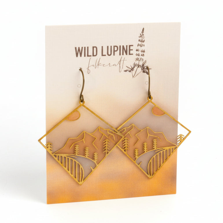 Pair of earrings with mountain and tree design on a 'Wild Lupine Folkcraft' card.