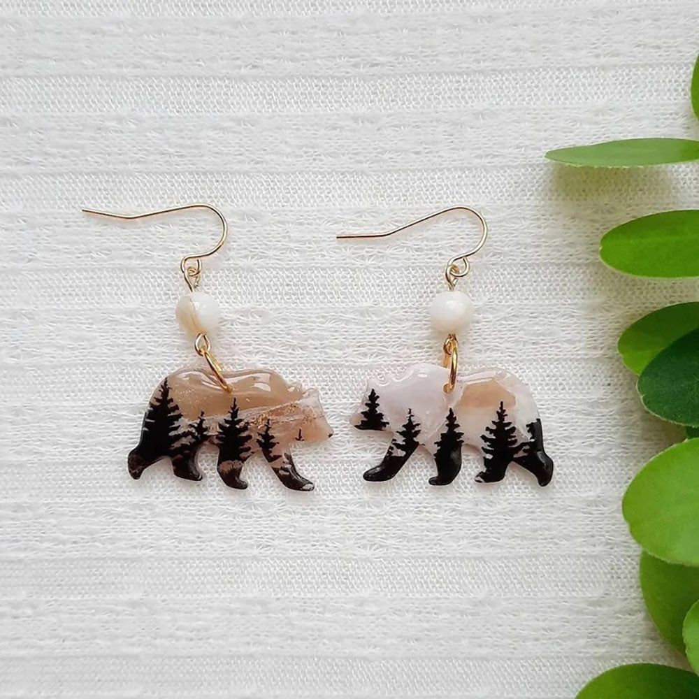 Pair of earrings with bear and pine tree design on a white background