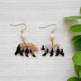 Pair of earrings with bear and pine tree design on a white background