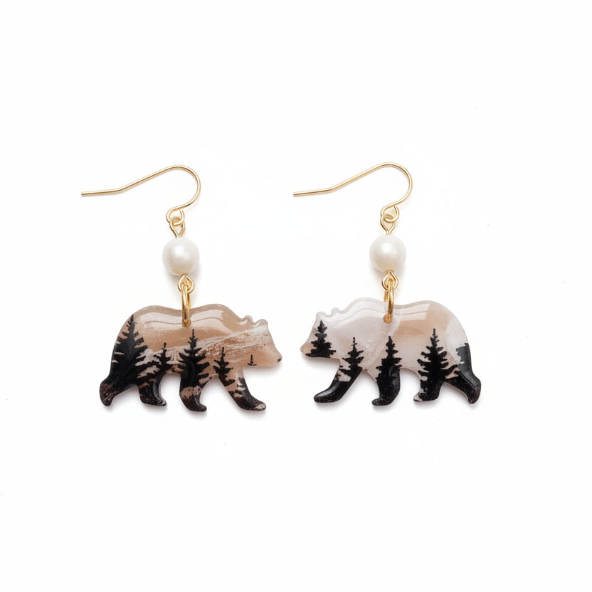 Pair of earrings with bear and pine tree design on a white background