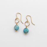 A pair of gold dangle earrings with round turquoise-blue marbled beads, displayed on a white surface.
