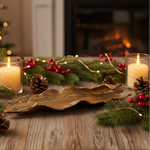 Decorative setting with candles, greenery, and a gold driftwood dish on a wooden surface.